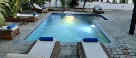A rectangular pool with lounge chairs and a tiled patio.