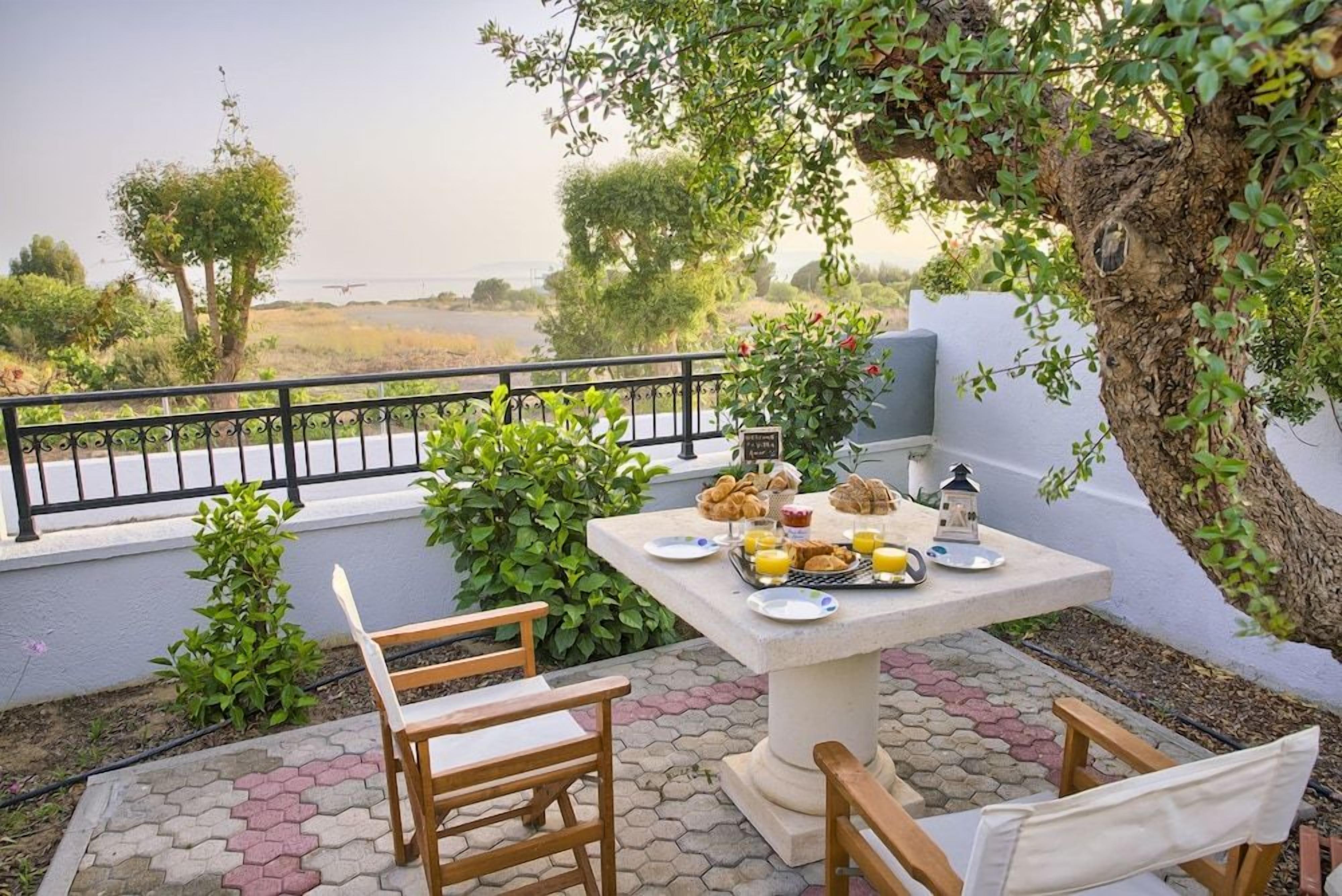 An outdoor dining area with a table set for breakfast, surrounded by greenery and overlooking a scenic landscape.