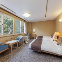Habitación de hotel con cama, escritorio, silla, mesita y ventana con vistas a árboles.