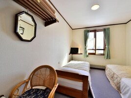 A room with two beds, a chair, a desk, a mirror, and a window with curtains.