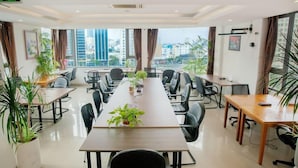 Uma sala de conferências com uma mesa comprida, várias cadeiras e plantas em vasos.