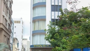 Um edifício alto de hotel com uma placa no topo indicando 'WAIKI BEACH HOTEL'.