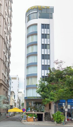 Un grand immeuble d’hôtel, sur lequel on peut lire au sommet l’inscription « WAIKI BEACH HOTEL ».