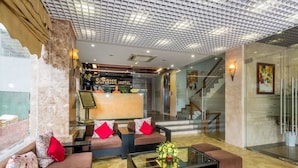 Um saguão de hotel com balcão de recepção, sofás, mesa de centro e escada.