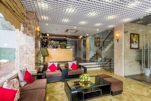 Un hall d’hôtel comprenant un comptoir d’accueil, des canapés, une table basse et un escalier.