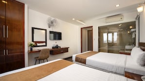 Quarto de hotel com duas camas, uma mesa, uma cadeira, uma TV e banheiro com chuveiro de vidro.