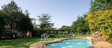 A swimming pool with a stone edge, surrounded by grass and trees.