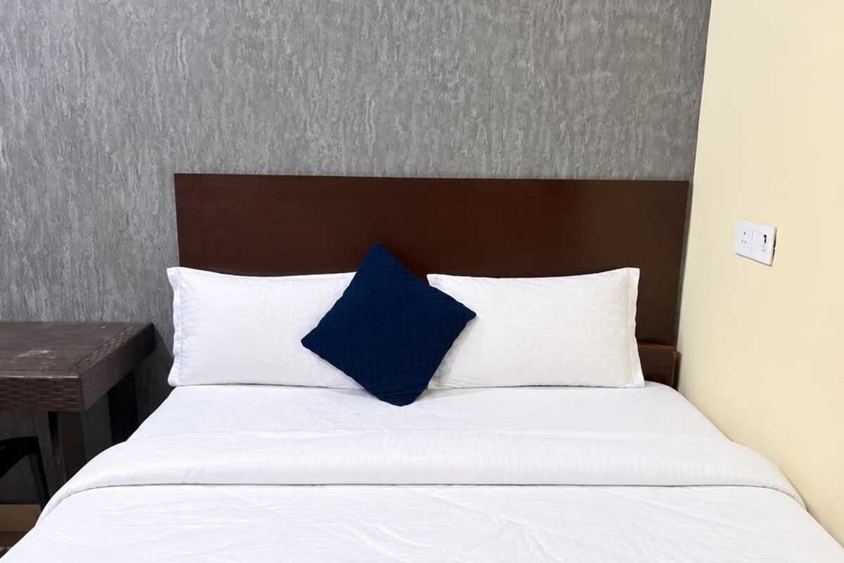 A neatly made bed with white bedding and a single blue accent pillow, a wooden headboard, and a nightstand with a lamp.