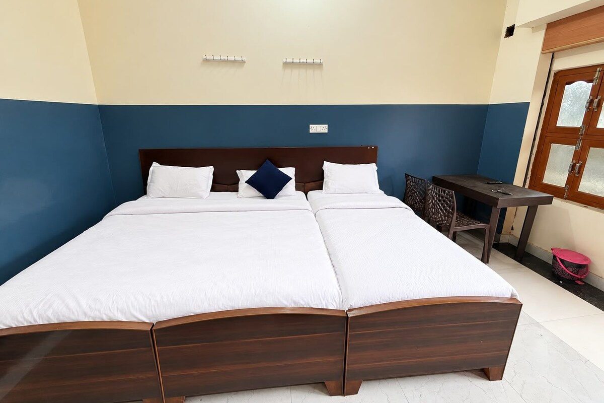 A double bed with a wooden frame, two bedside tables, a small table, and a chair in a room with blue and beige walls.