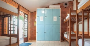 Une chambre avec des lits superposés, une armoire bleue et un ventilateur.
