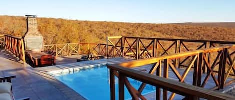 A pool area with a wooden deck and metal railings, surrounded by a natural landscape.