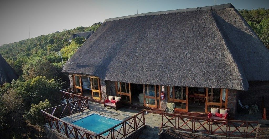 A thatched-roof building with a pool, wooden deck, and outdoor seating.
