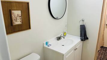 A bathroom with a white sink, a mirror, a framed picture, and a towel rack.