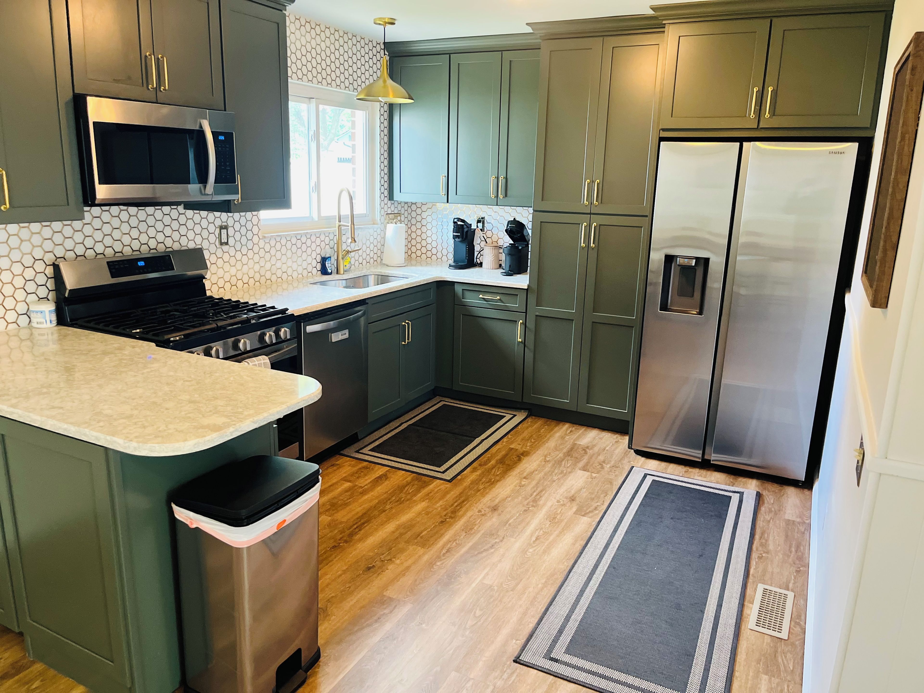 A modern kitchen with dark green cabinets, stainless steel appliances, and a marble countertop.