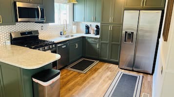 A modern kitchen with dark green cabinets, stainless steel appliances, and a marble countertop.