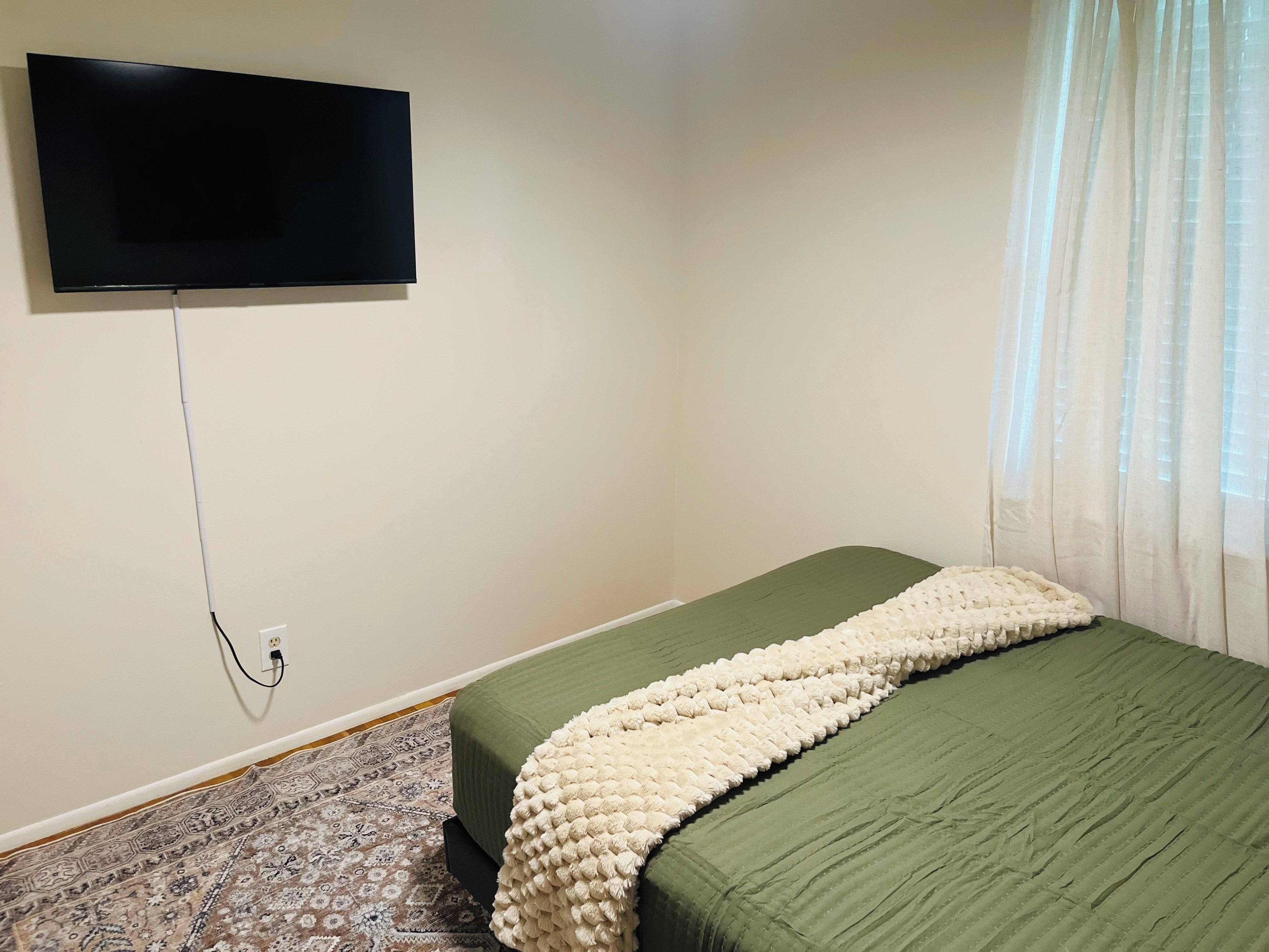 Quarto com cama, televisão na parede e tapete estampado.