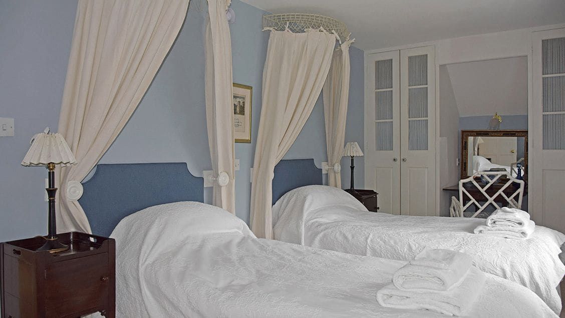 A bedroom with two beds, a nightstand, a mirror, and a wardrobe.