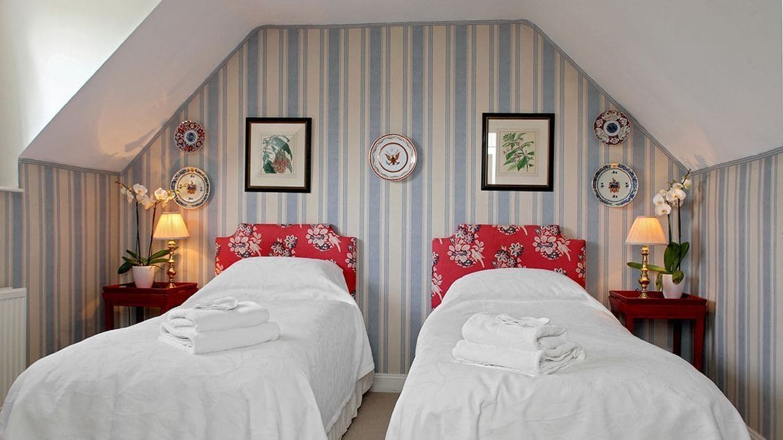 A room with two beds, striped wallpaper, and decorative plates on the wall.