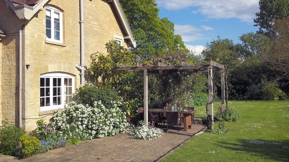 A stone building with a garden patio, a pergola, and a lawn.
