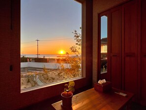 Ein Zimmer mit großem Fenster und Blick auf einen Sonnenuntergang, einem Holztisch und einer kleinen Pflanze.