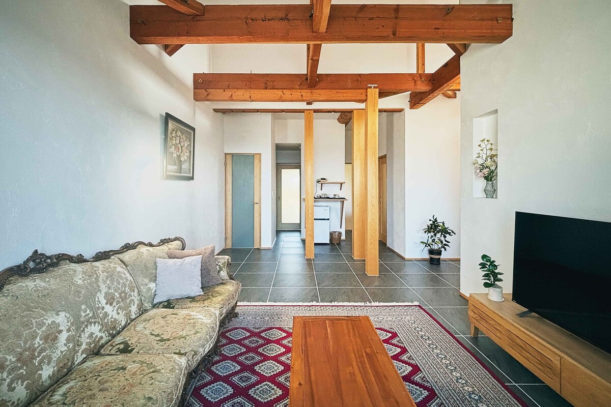 Ein Wohnzimmer mit einer Couch, einem Couchtisch, einem Fernseher und einer Küche im Hintergrund.