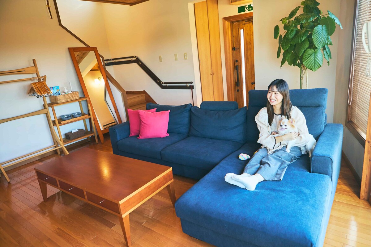 Ein Wohnzimmer mit einem blauen Sofa, einem Holztisch, einer Treppe und einer Topfpflanze.