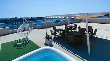Ein Außenpoolbereich mit Meerblick, umgeben von Sitzgelegenheiten und einer Pergola.
