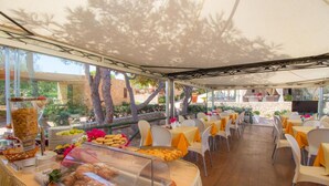 An outdoor dining area with tables and chairs, a buffet with food items, and a view of the surrounding landscape. - Residence Luna Di Ponente (Lampedusa)