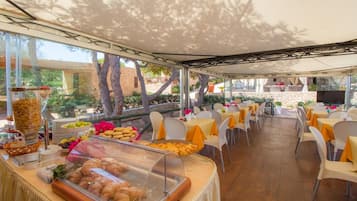Ein Außenbereich zum Essen mit Tischen und Stühlen, ein Buffet mit Speisen und Blick auf die umliegende Landschaft.