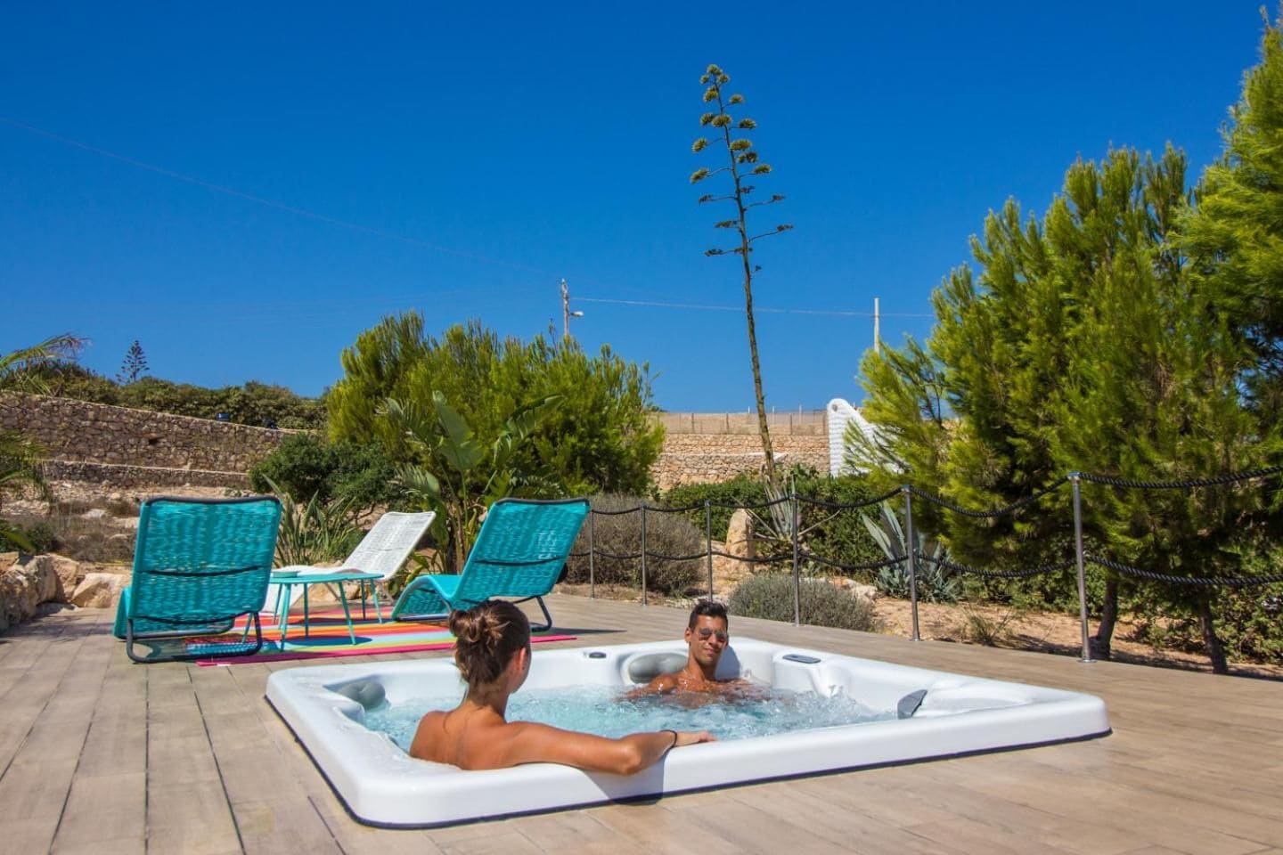 A hot tub with two people, surrounded by outdoor seating and greenery.