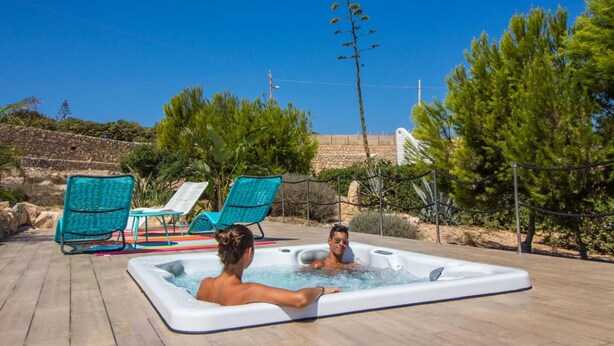A hot tub with two people, surrounded by outdoor seating and greenery. - Residence Luna Di Ponente (Lampedusa)