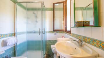Ein Badezimmer mit Duschkabine aus Glas, Waschbecken, Toilette und Spiegel.