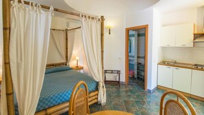 A room with a bed, a table, a chair, a kitchen area, and a bathroom visible through an open door. - Residence Luna Di Ponente (Lampedusa)
