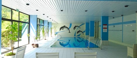 An indoor swimming pool with dolphin murals, white chairs, and a blue and white color scheme.
