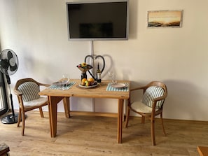 Una mesa de comedor con sillas, un televisor montado en la pared y un cuadro enmarcado.