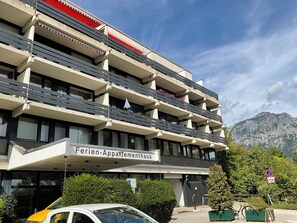 Un hotel de varios pisos con balcones, un cartel que dice 'Ferien-Appartementhaus' y un paisaje de montaña al fondo.