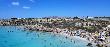 A beach with clear turquoise water, rocky terrain, and a mountainous backdrop.