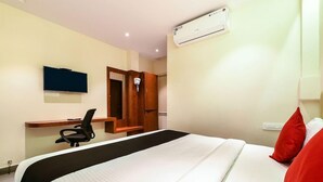 A hotel room with a bed, a desk, a chair, a TV, and an air conditioning unit. - Capital O 22922 Hotel Siddartha Grand (Vijayawada)