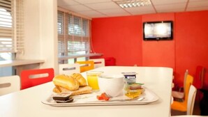 A breakfast tray with croissants, orange juice, and yogurt on a white table in a room with red walls and a television mounted on the wall.