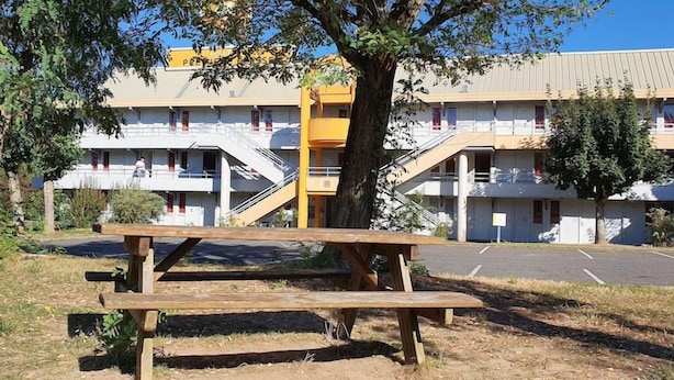 A multi-story building with a parking lot, a picnic table, and a tree in the foreground.