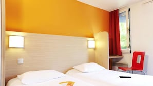 A hotel room with two beds, a red chair, and a window with curtains.