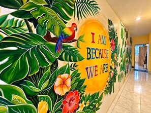 A hallway with a mural featuring tropical plants and a parrot, and the text 'I AM BECAUSE WE ARE'. - Ubuntu Live Boutique Hostel & Rooms (Phuket)