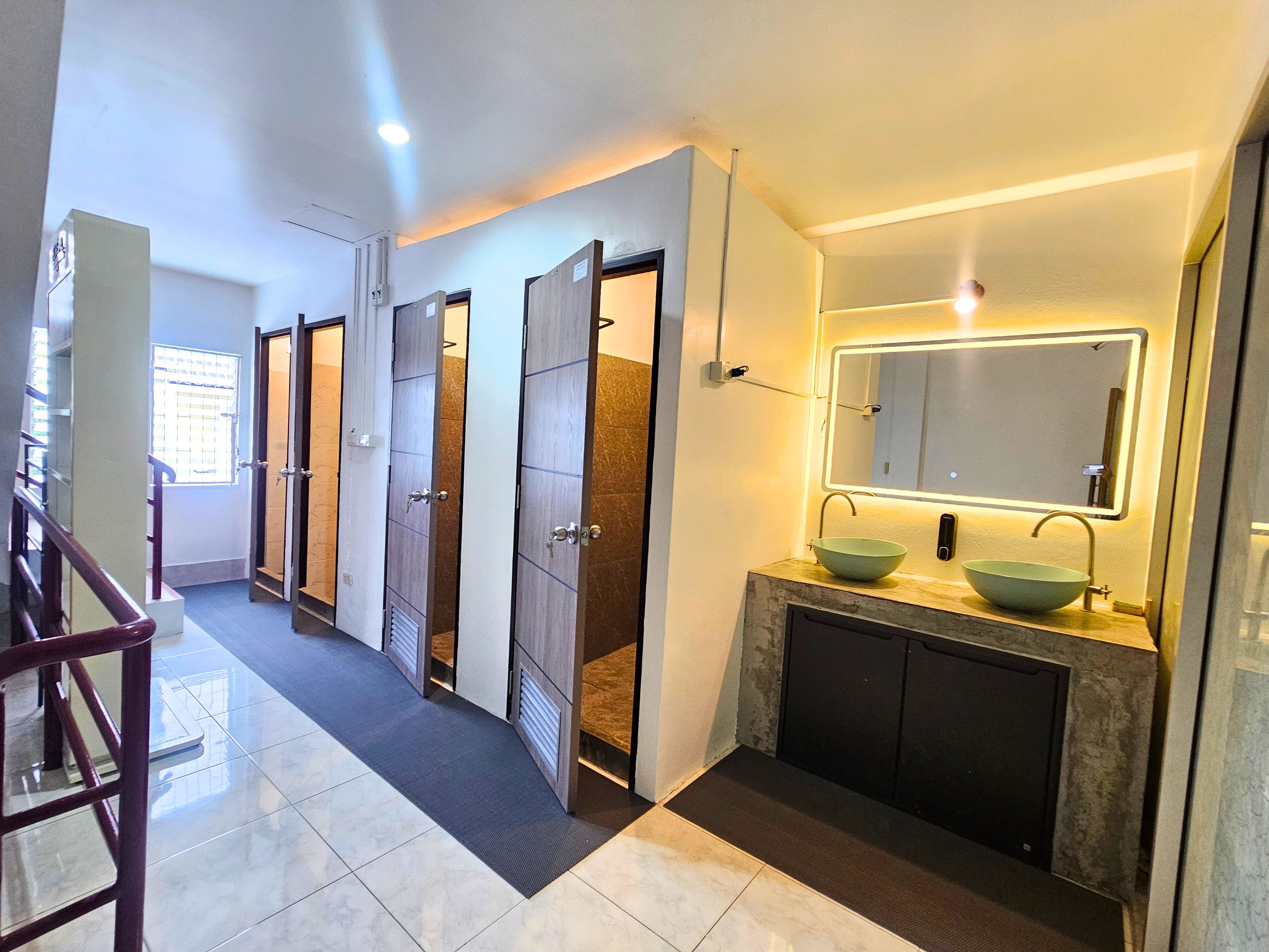 Un baño de hotel con diseño moderno, que incluye un espejo grande, dos lavamanos y piso de baldosas.