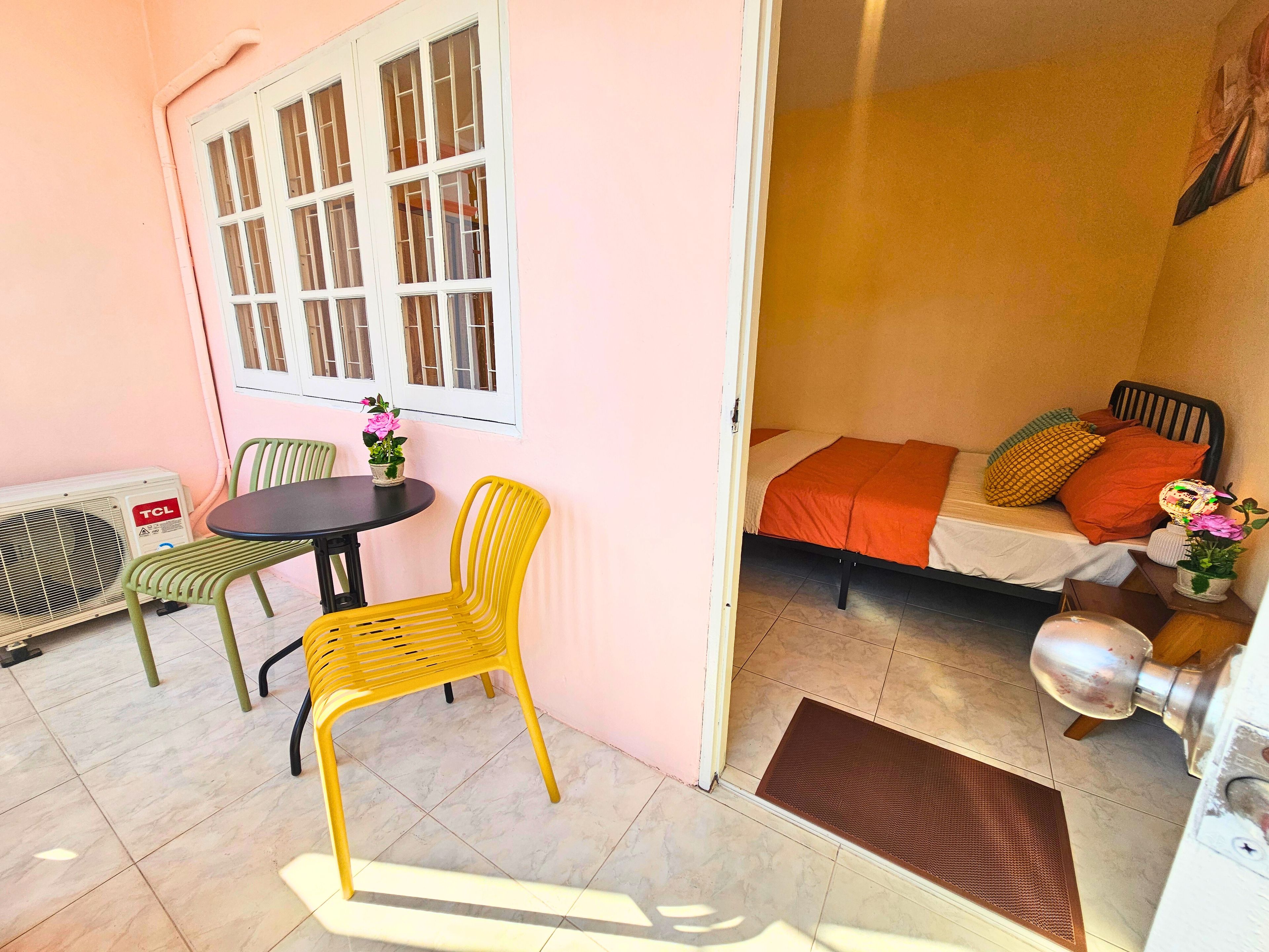 A room with a bed, a table, and chairs. There is a window with bars and a radiator.