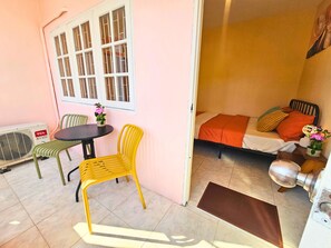 A room with a bed, a table, and chairs. There is a window with bars and a radiator.