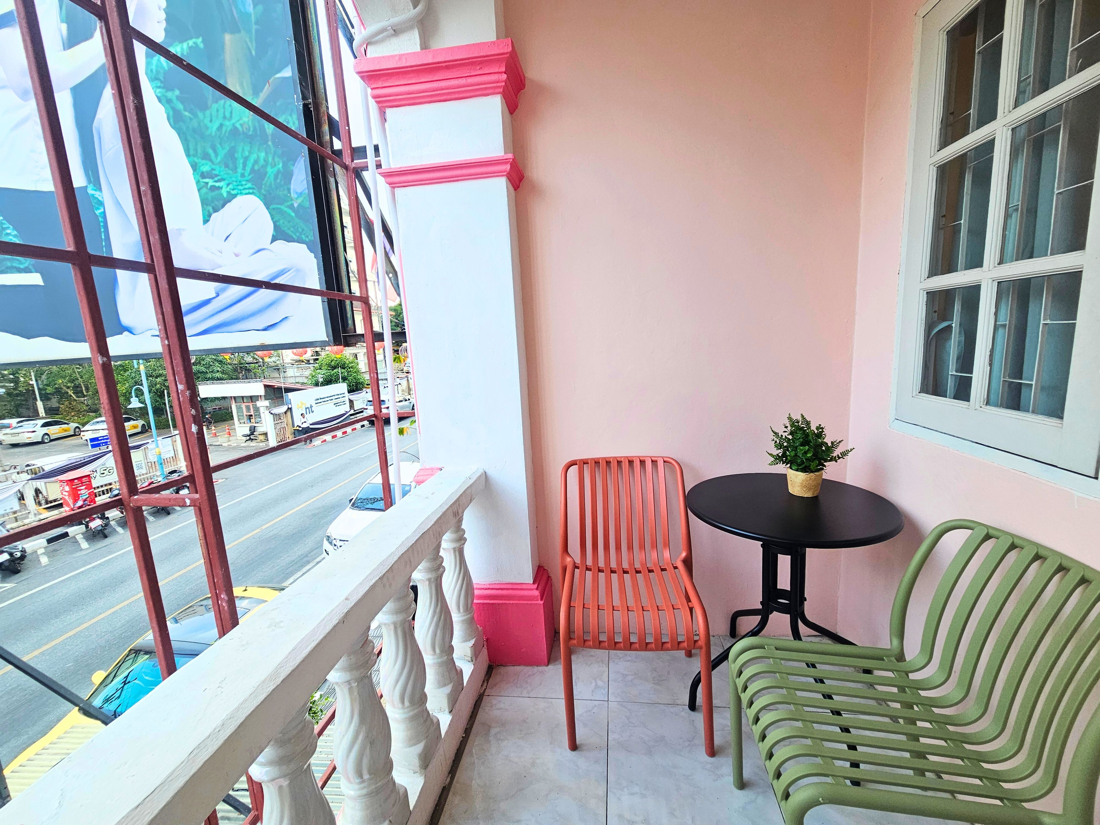 A balcony with a view of a street, a small table with a plant, and two chairs.