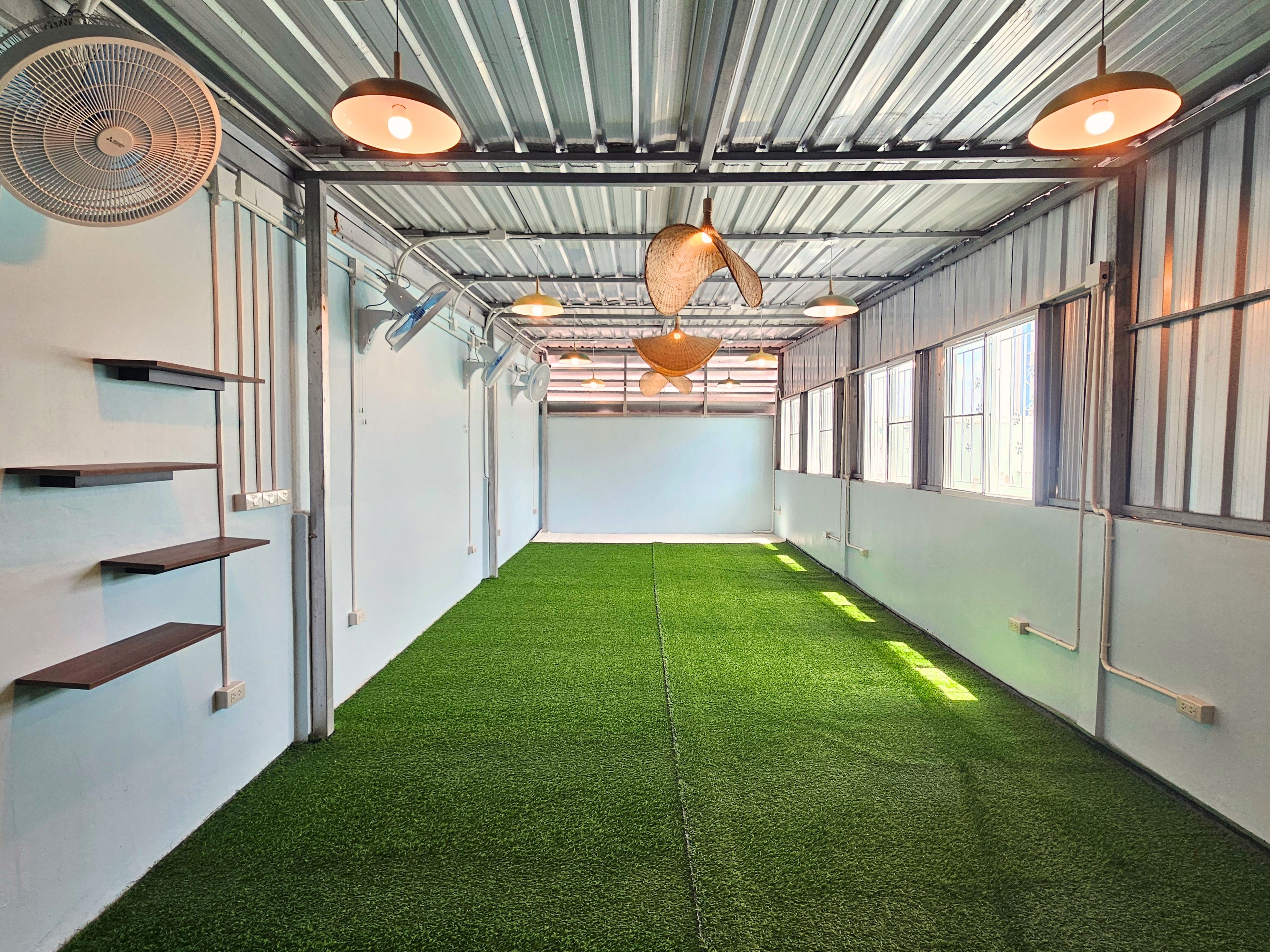A hallway with artificial green flooring, metal shelving units, and pendant lighting.