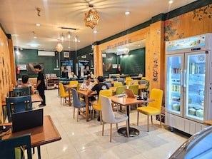 A restaurant interior with tables, chairs, and a refrigerator stocked with beverages. - Ubuntu Live Boutique Hostel & Rooms (Phuket)