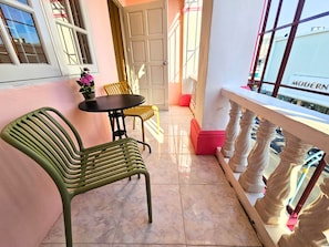 A balcony with a table and chairs, a potted plant, and a view of a building with the word 'MODERN' on it.