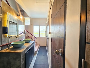 A bathroom with a sink, mirror, and a wooden door. - Ubuntu Live Boutique Hostel & Rooms (Phuket)